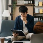 Frustrated young businessman working on a laptop computer sitting at his working place in home office - The MortgagePoint