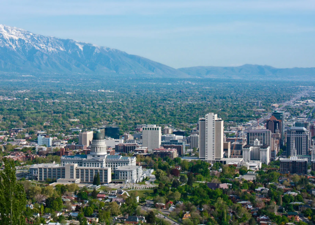 City skyline with a domed capitol building in the foreground and snow-capped mountains in the distance