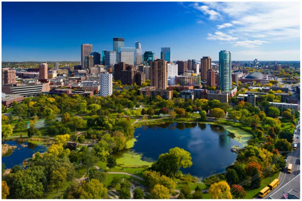 Aerial view of downtown skyline with tall buildings behind a large green park and a circular lake in the foreground.